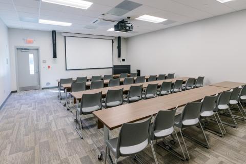 Meeting Room B set up in rows of desks and chairs with the projector screen lowered at the front of the room.