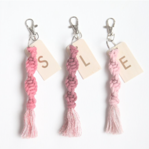 Three macrame keychains in varying pink colors with the initials S, L, and E.